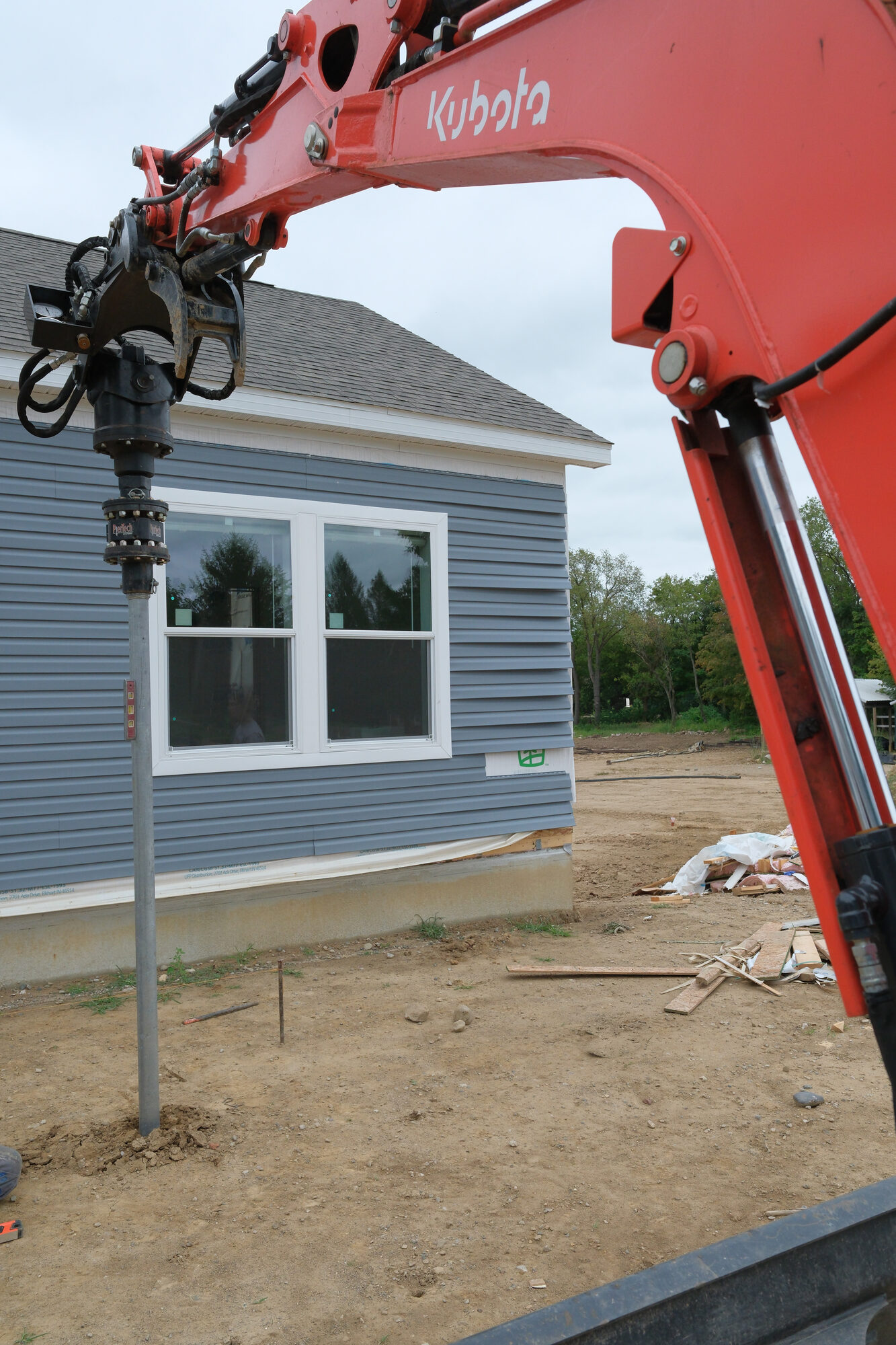Helical pier being installed directly beside a house foundation under a window
